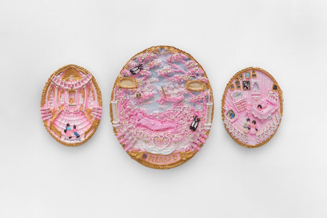 Three oval-shaped artworks hang on a white wall. They are all gorgeously pink and white, with gold frames. These lush, drippy pictures look as if they have been piped onto the ovals like cake frosting. Each one represents a small scene where people visit a grand hall, recline on beds of beautiful flowers, or pray in a bedroom.