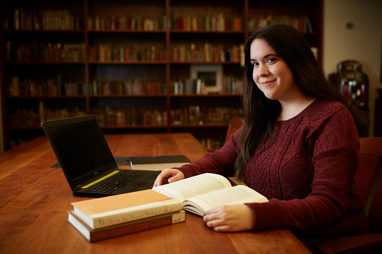 A student in the library with her literature books and her computer open.
