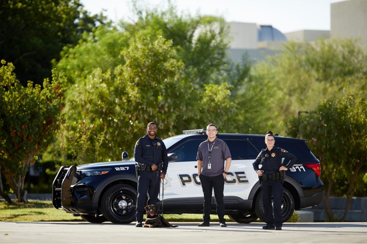 Three university police employees and a k-9 officer posing next to a police S-U-V
