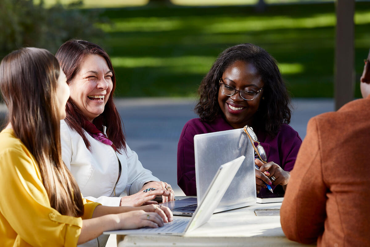 A group of four people sitting down outside at table with a laptop