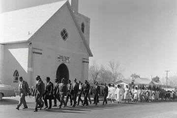 archival photo of large group walking in front of church