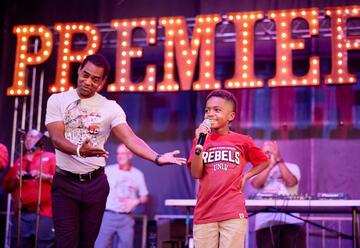 boy with microphone on stage with man pointing to boy