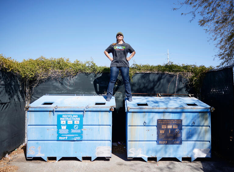 woman standing atop two closed dumpsters