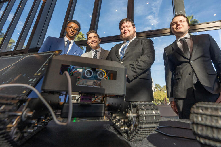 four students in suits in front of equipment