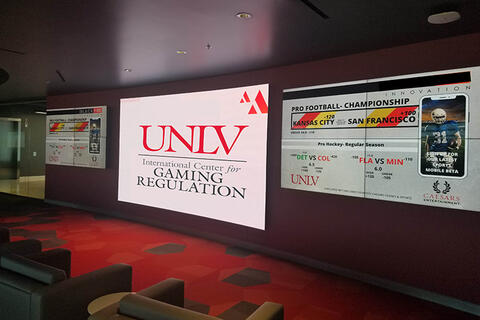 A room with the UNLV Gaming Regulation and scores of pro football championship on games on projector.