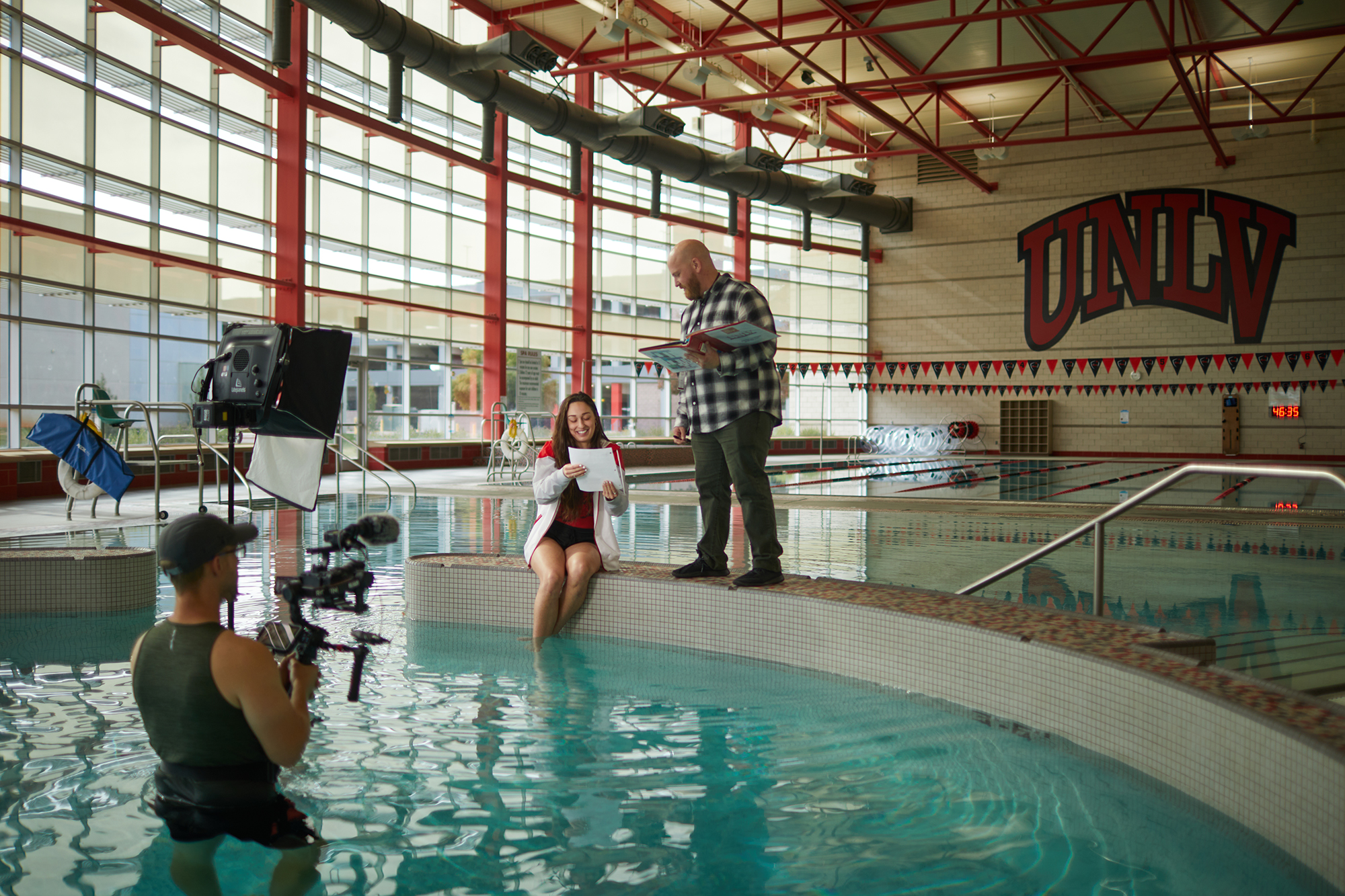 Two people in pool with another person standing on the side.