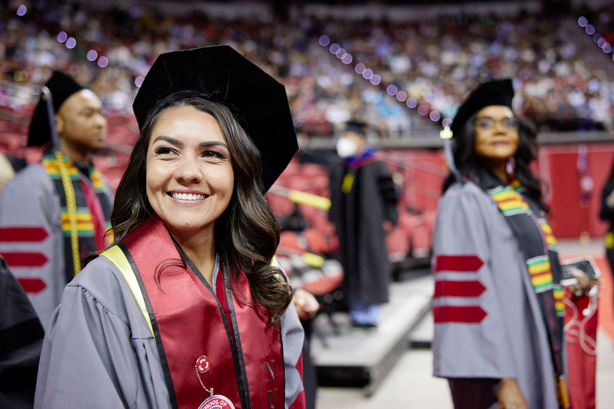 Students standing on the main floor of the graduation commencement ceremony, staring in the distance.