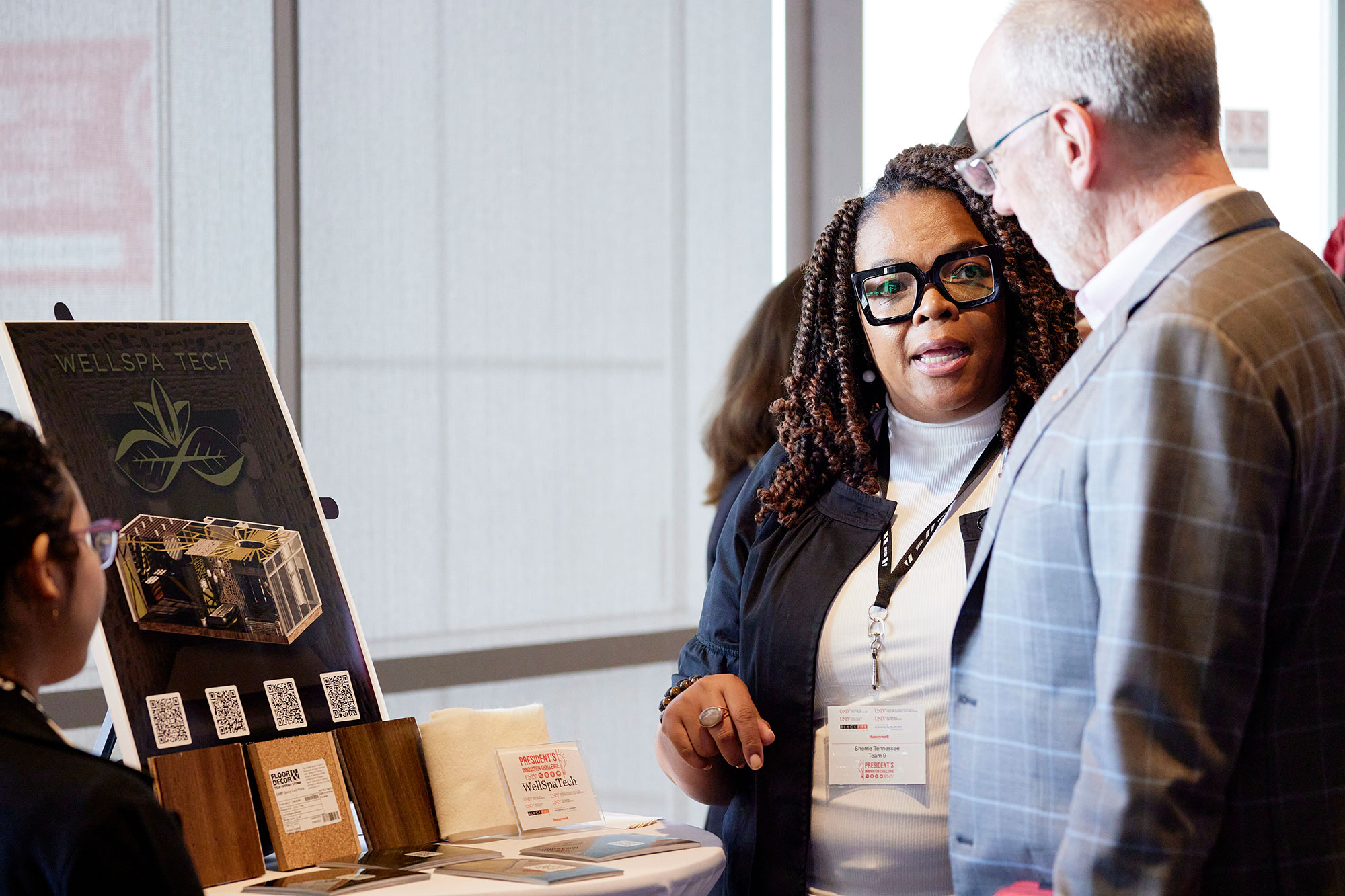 A man and woman having a conversation in front of a presentation stand with different types of textiles