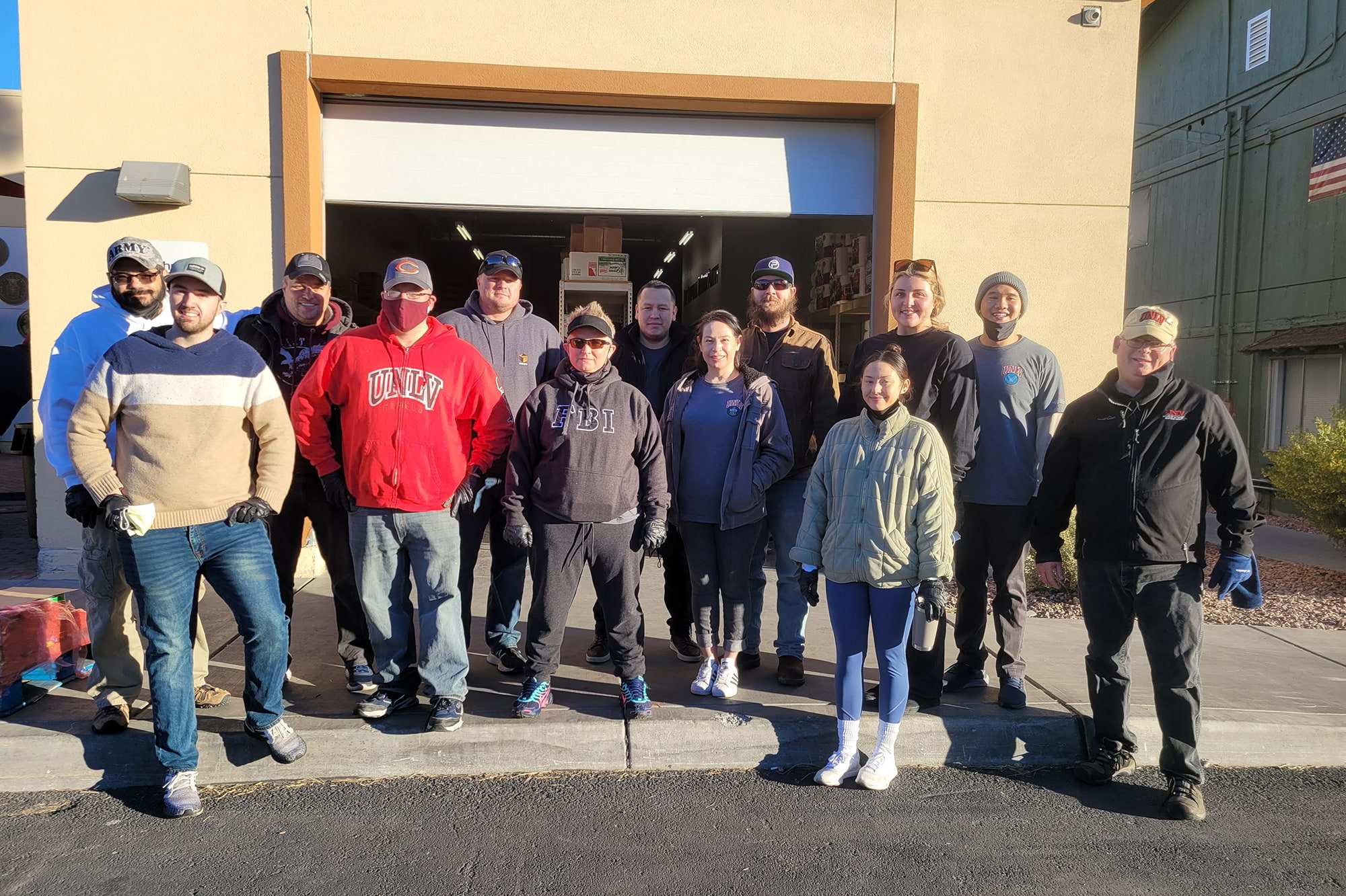 A group of 13 people, smiling in front of a storage building