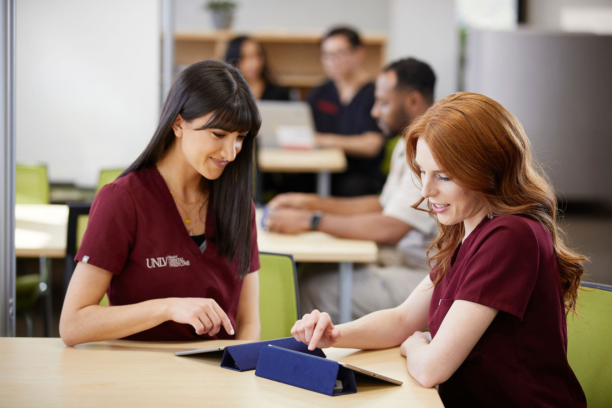 Two women in scrubs looking at their tablet