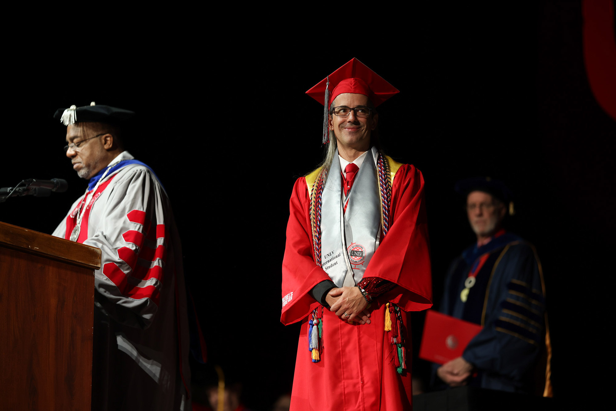 A man at a graduation ceremony holding their hands together on stage