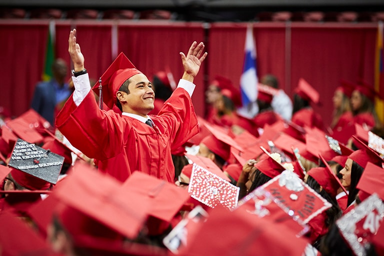 Student stands with hands in the air during commencement.