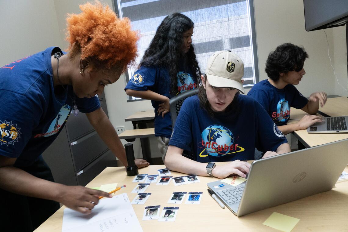 Four students gather around laptops in an office on UNLV's campus to solve clues in a cybersecurity escape room.