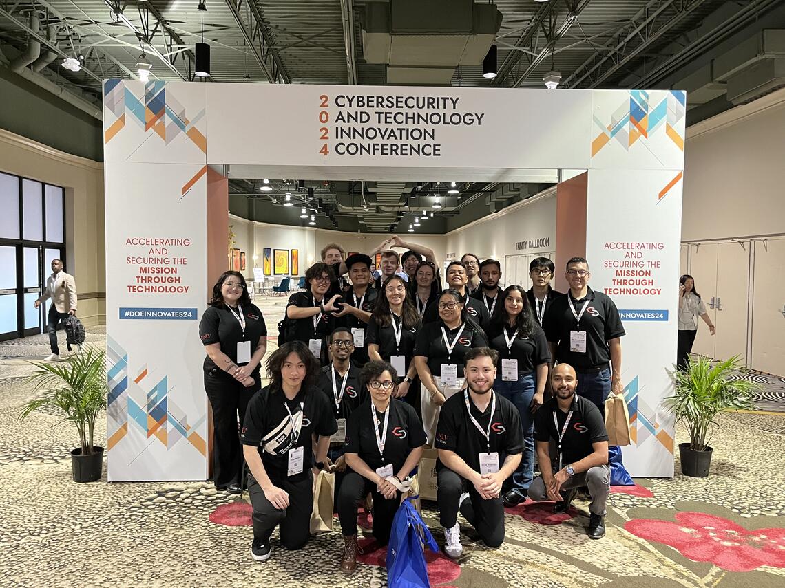 A large group of people post for a photo under a big archway at a convention center