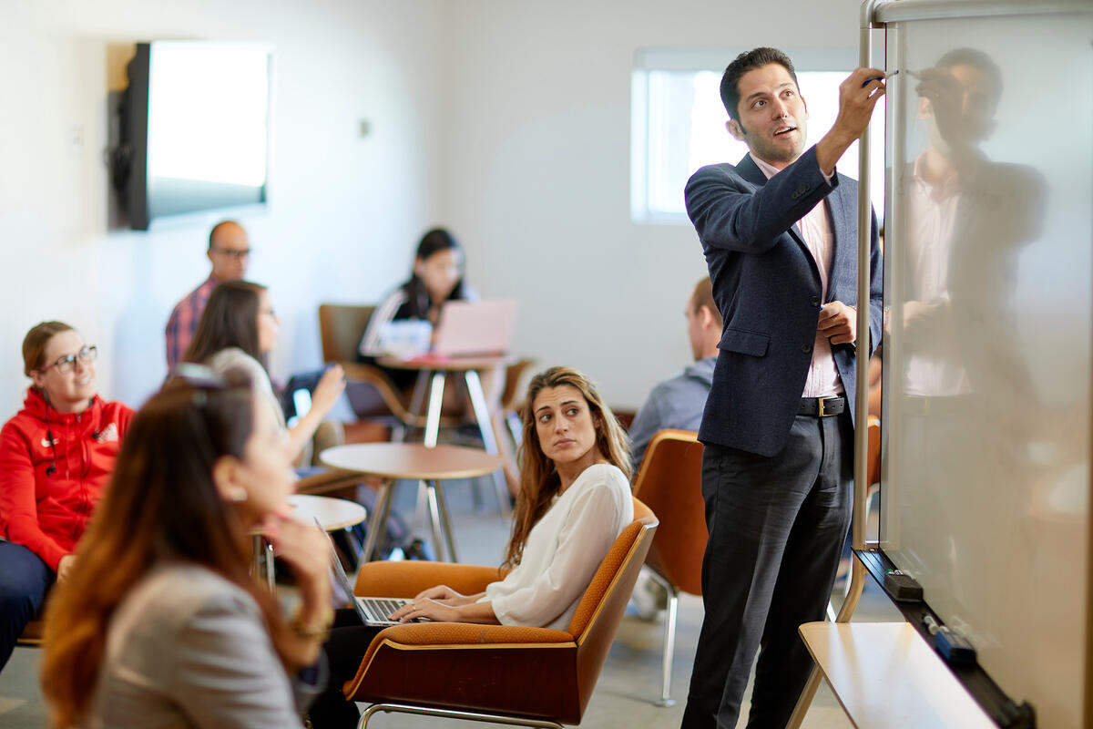 Man standing at a white board a lecturing a small class