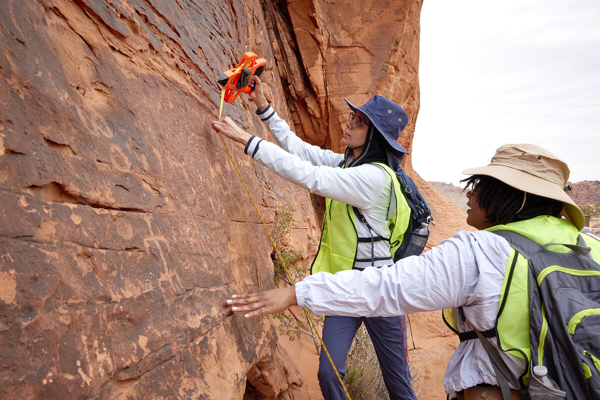 two students measure the surface of a large rock