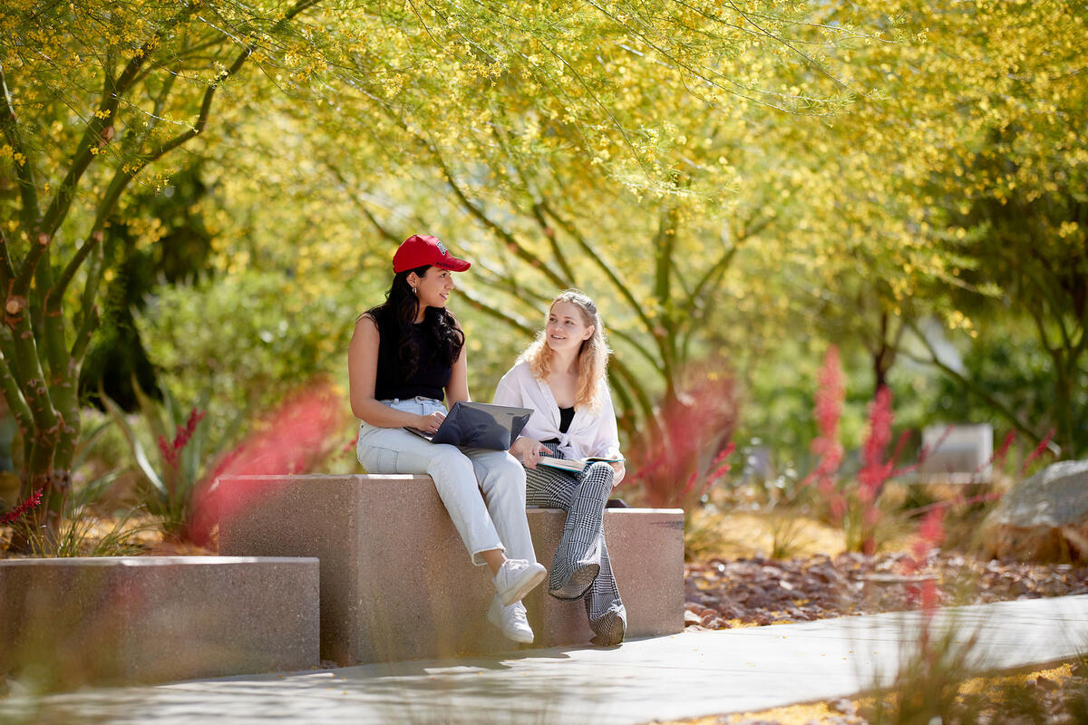Two people sitting down on a block bench with trees surrounding them
