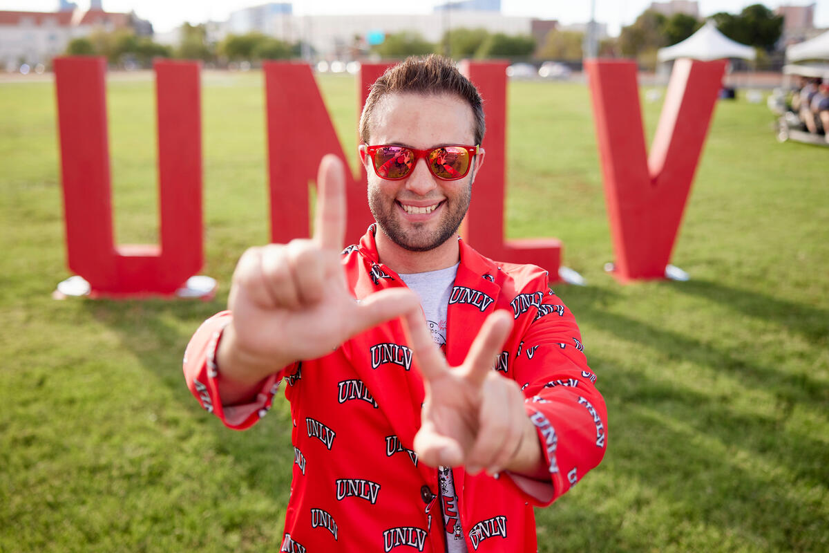 man wearing UNLV jacket making 'LV' sign with hands