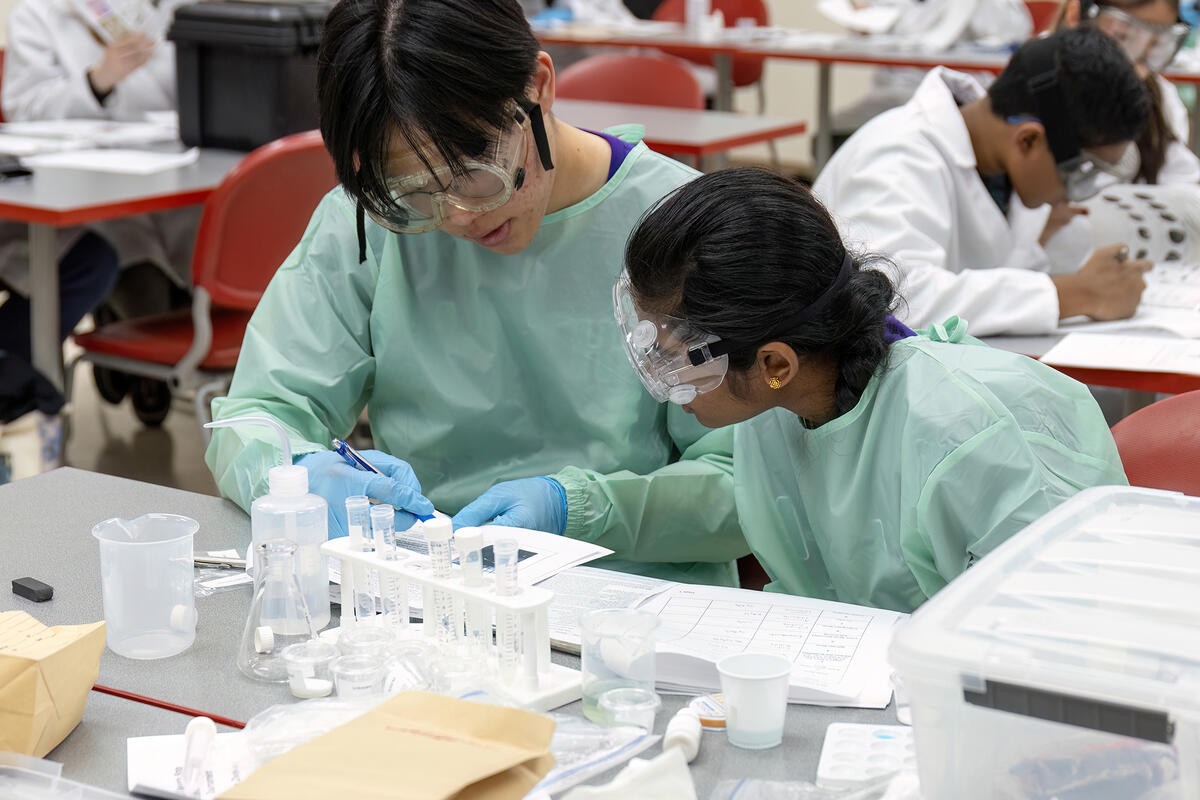 college and k-12 student wearing scrubs while working on experiment