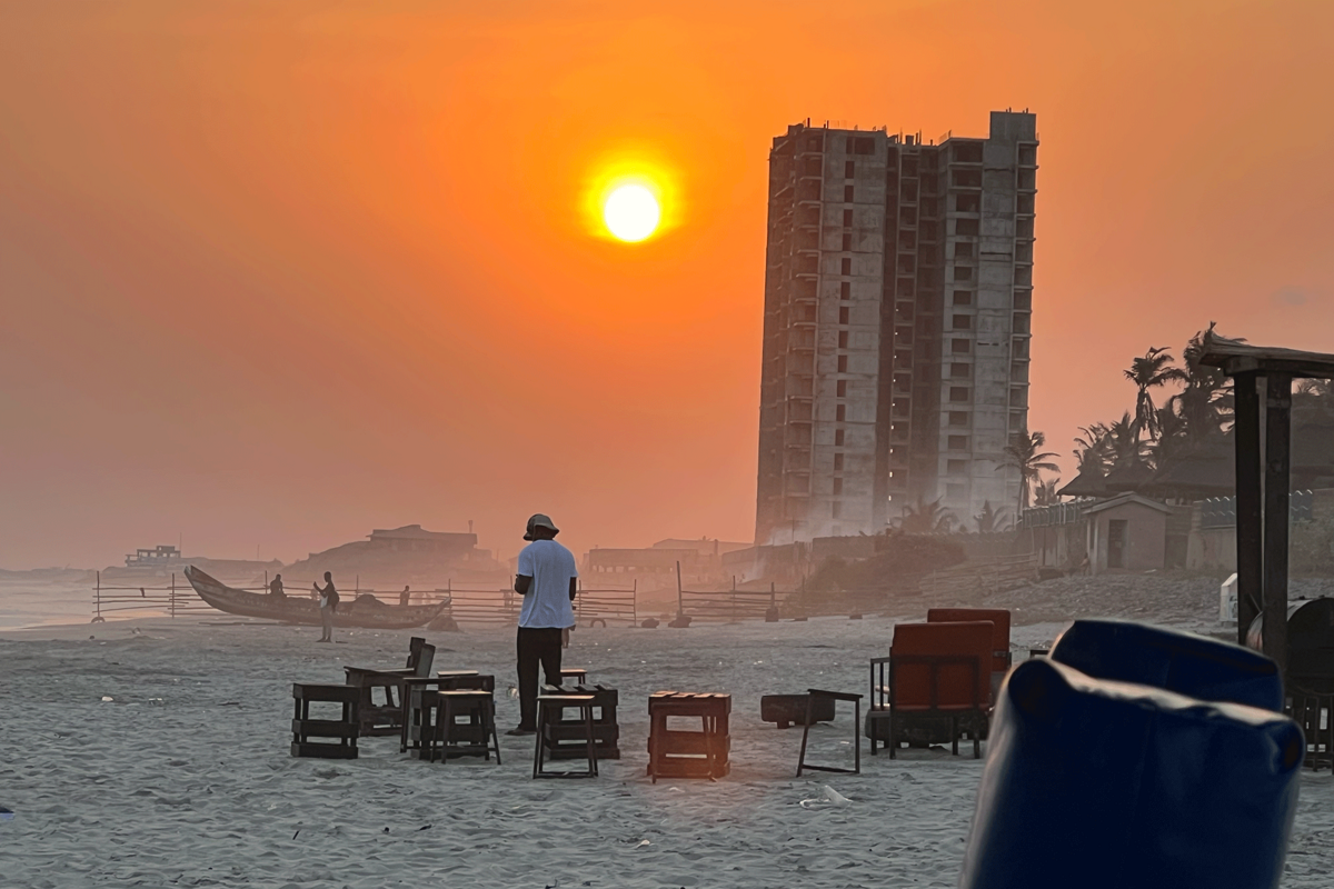 Sandy beach with an orange sun in the background and a lone man standing at the center of the photo