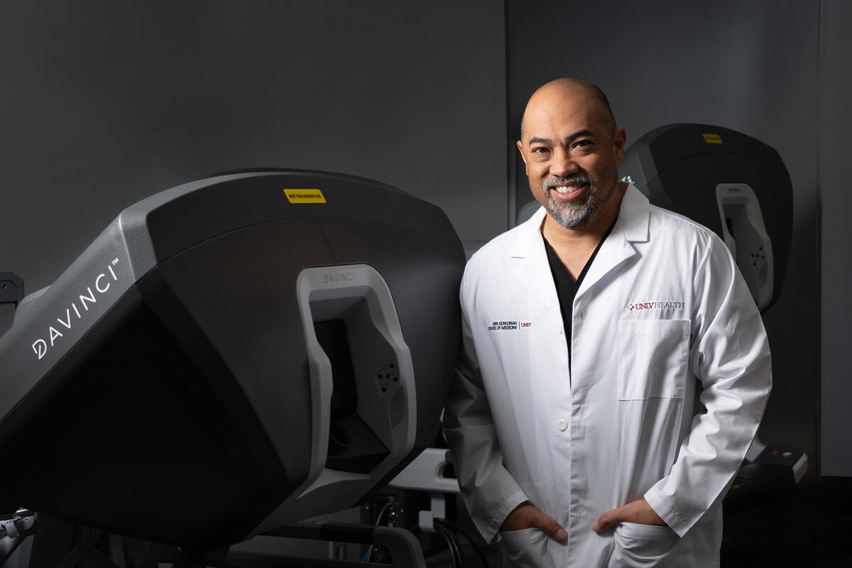 Portrait of Richard Baynosa standing next to a surgical robot.