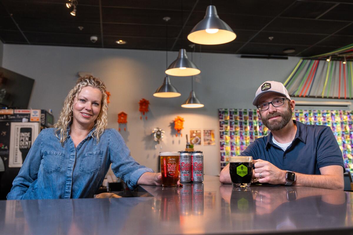 From left, Wyndee Forest and Dave Forrest each hold beers while seated at a table at their CraftHaus Brewery