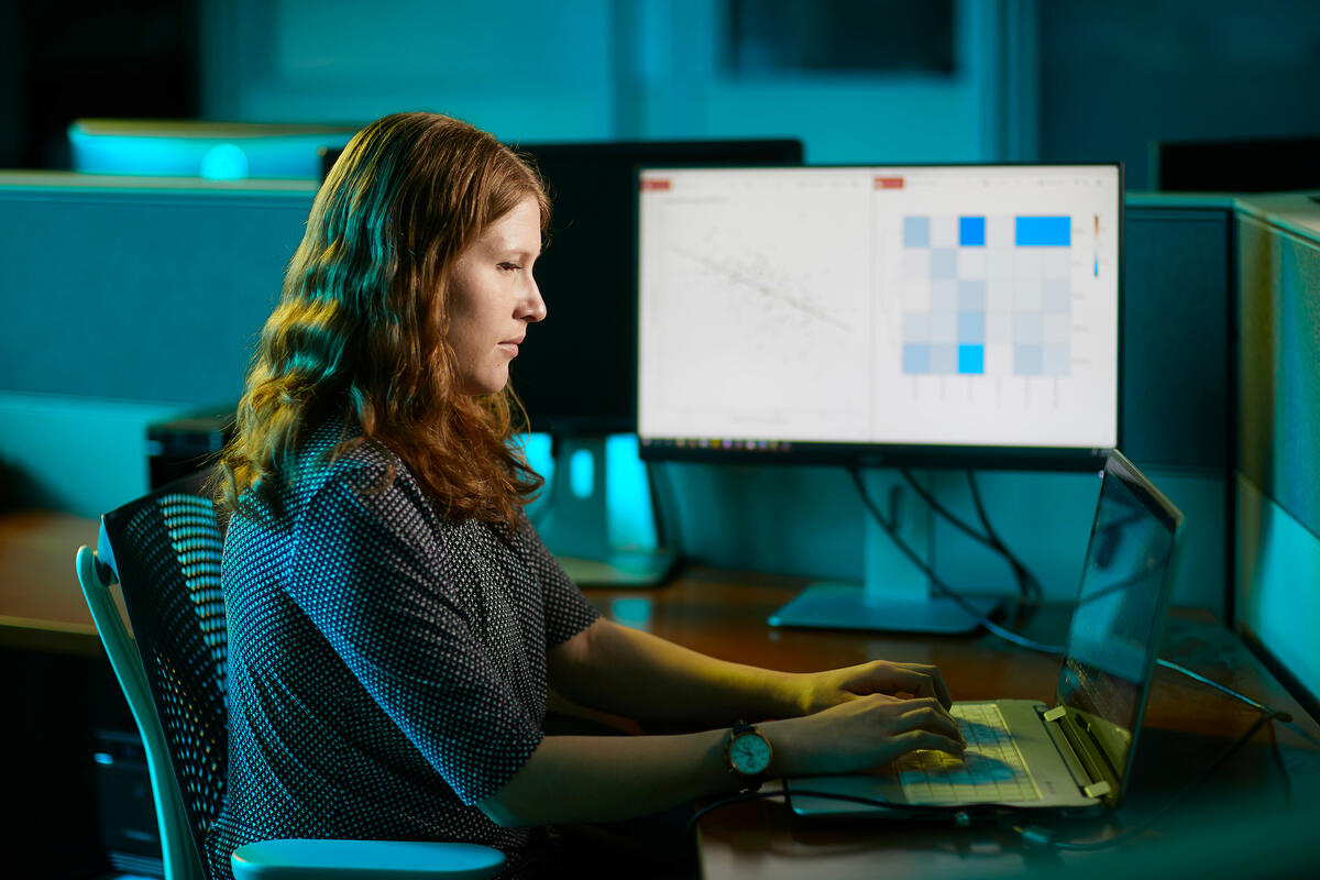 woman at computer with screen beside her showing graphs