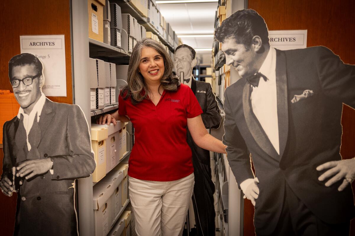 Su Kim Chung poses with cardboard cutouts of Sammy Davis Jr. Frank Sinatra and Dean Martin in the UNLV Special Collections and Archives office