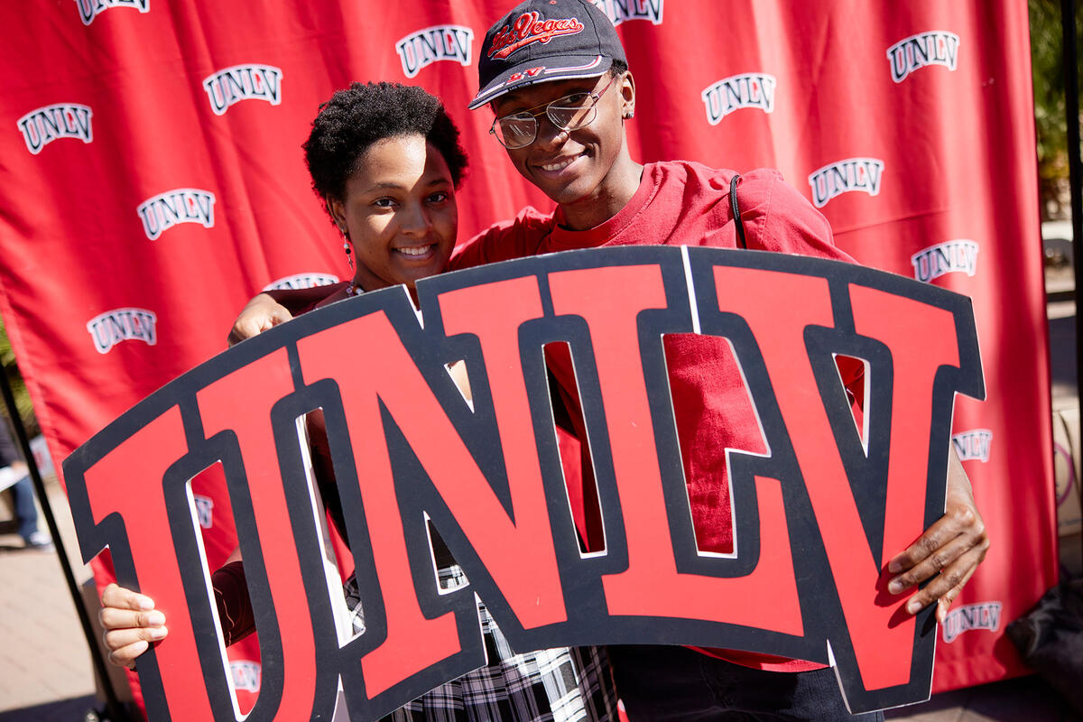 Two people holding an U-N-L-V sign with a backdrop