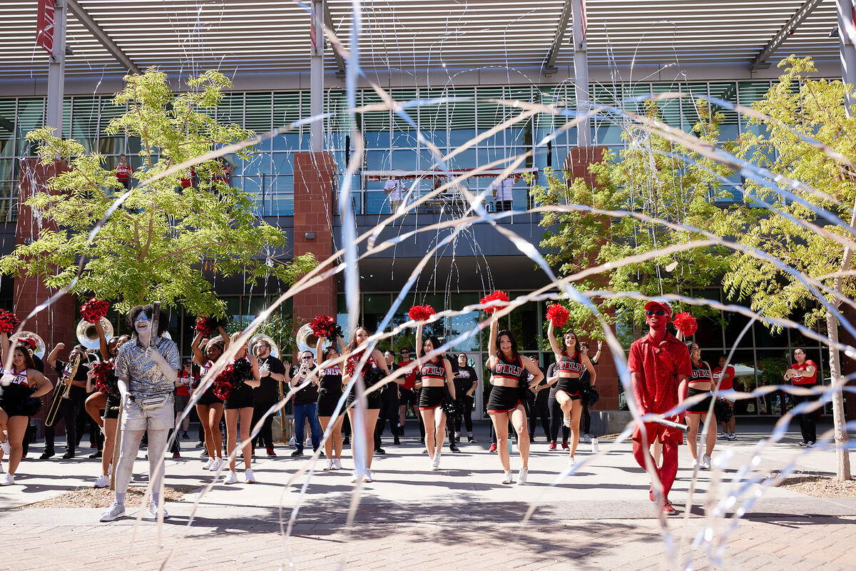 Cheerleaders dancing and one person on each side dressed in red and silver glitter