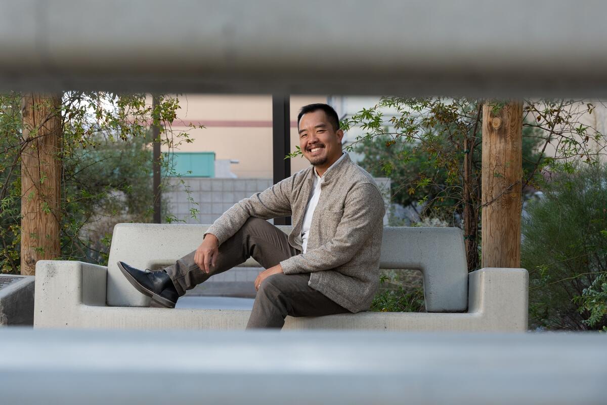 UNLV professor Federick Ngo on campus while sitting on a bench with his right raised and his right foot on the bench