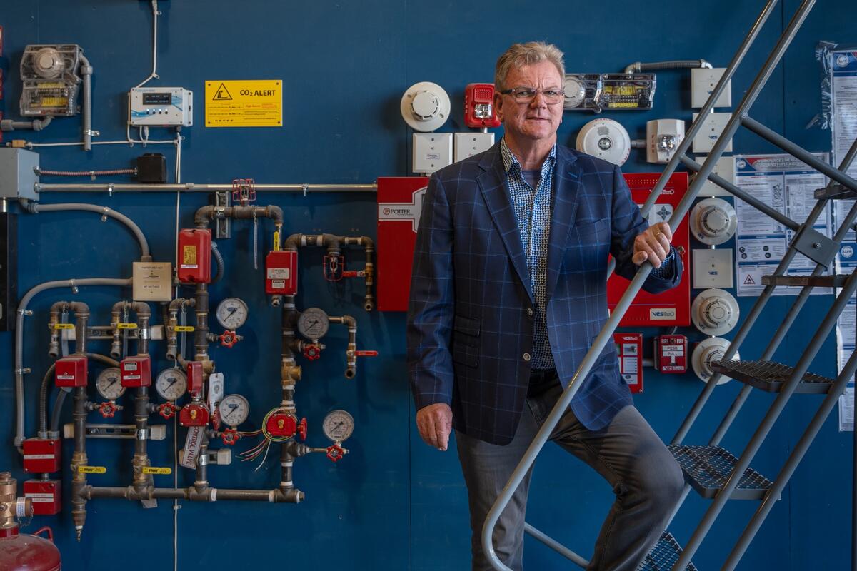 Wearing a blue checkered blazer, blue checkered dress shirt and gray pants, Joe Murphy, winner of the 2024 Silver State Award, poses in the shop at Murphy Electric