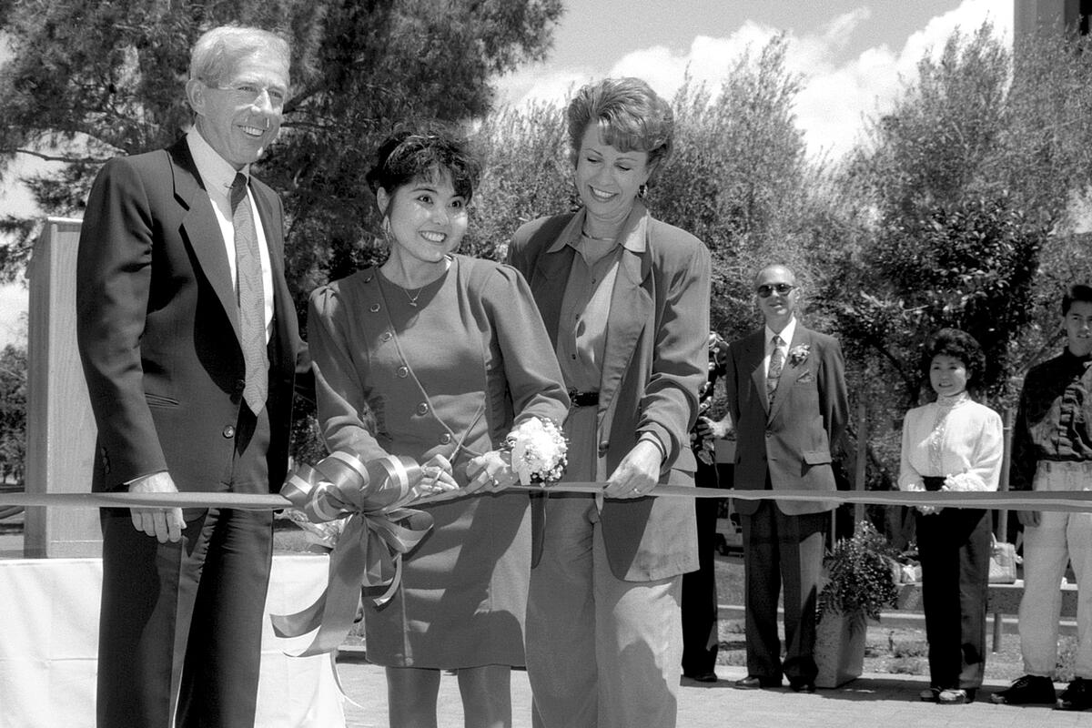 a man and two women cutting a ribbon outdoors