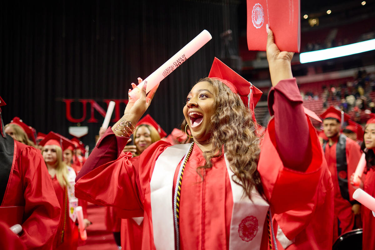 An excited woman at graduation holding up a program book and lightstick