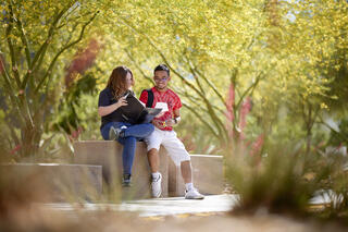 two students looking at a binder outdoors with green trees