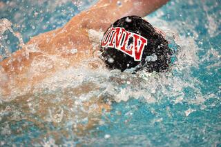 A student-athlete swimmer in the pool wearing a UNLV swim cap.