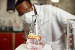 A student in a lab with a radioactive flask.