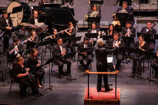 The UNLV Wind Orchestra is on the Artemus W. Ham Concert Hall Stage; Thom Leslie, the conductor, is conducting the orchestra.