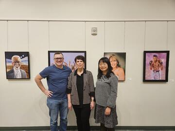 three individuals pose together in front of wall with framed art behind them