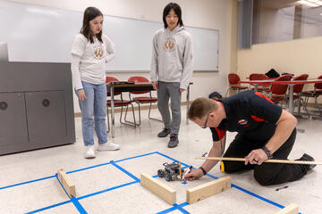 two young students observe man marking floor during experiment