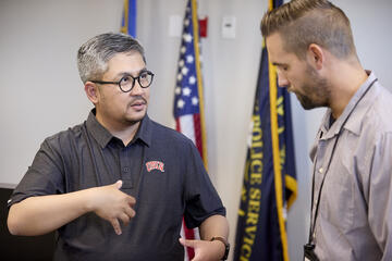 two men talking with flags behind them