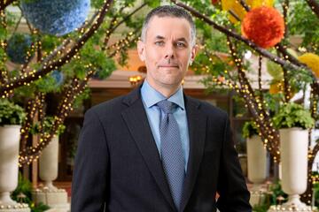 Wynn Las Vegas CEO Craig Billings poses in a dark blue suit in front of trees strung with white lights