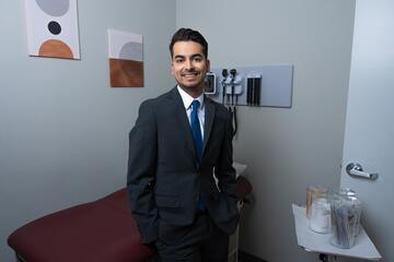 Fabian Doñate poses in a dark suit in a medical exam room