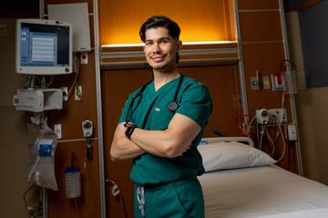 Physical therapist Juan Gutierrez poses with his arms folded in an empty hospital room