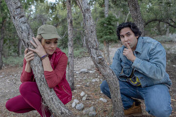 woman and man crouching behind trees