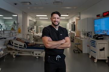 Wearing black medical scrubs, Dr. Chase Shropshire poses with his arms crossed in a mock hospital triage area at the UNLV School of Medicine