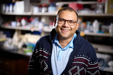 man in sweater and glasses in front of shelves inside lab