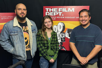 a woman and two men standing in front of a Film Department poster