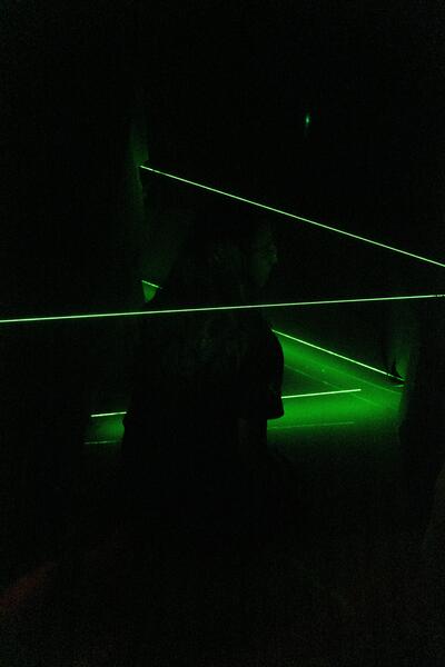 Students navigate a dark room with green lasers during a cybersecurity escape room challenge.