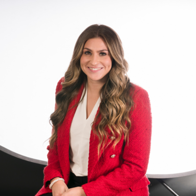 Headshot photo of Jozee Dean, lady with a white shirt and red jacket sitting while smiling.